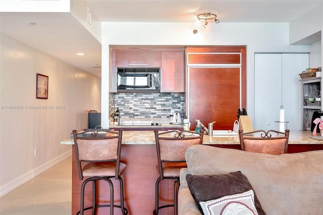 kitchen featuring decorative backsplash, light stone counters, a breakfast bar, and light hardwood / wood-style flooring