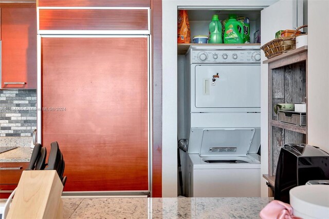 kitchen featuring decorative backsplash, light stone counters, and stacked washer and clothes dryer