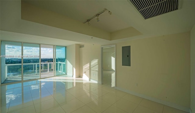 tiled empty room featuring electric panel and track lighting