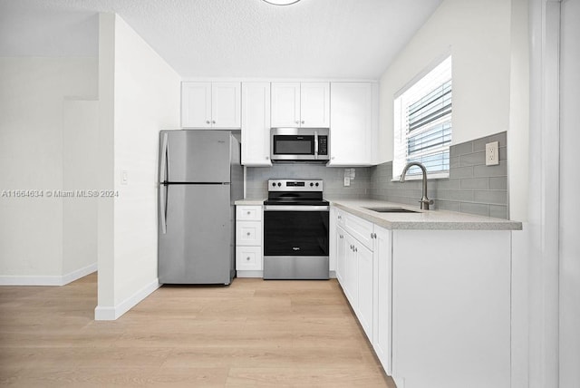 kitchen featuring sink, light hardwood / wood-style flooring, backsplash, white cabinetry, and stainless steel appliances