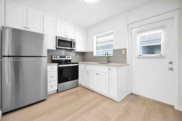 kitchen featuring sink, backsplash, white cabinetry, appliances with stainless steel finishes, and light wood-type flooring