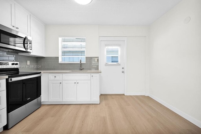 kitchen with appliances with stainless steel finishes, white cabinetry, tasteful backsplash, light wood-type flooring, and sink