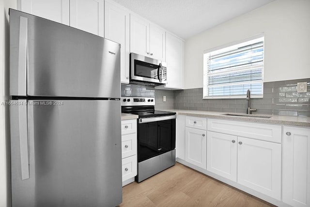 kitchen with sink, tasteful backsplash, light hardwood / wood-style flooring, white cabinetry, and appliances with stainless steel finishes