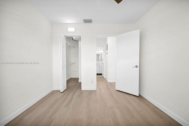 unfurnished bedroom with ceiling fan, light hardwood / wood-style flooring, a walk in closet, and a closet