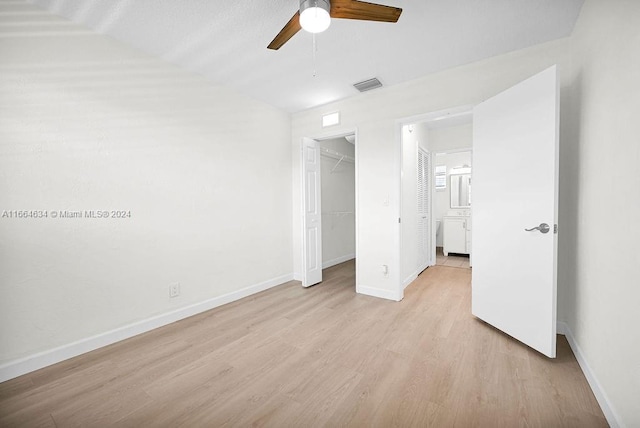 unfurnished bedroom featuring ceiling fan, lofted ceiling, light hardwood / wood-style flooring, a walk in closet, and a closet