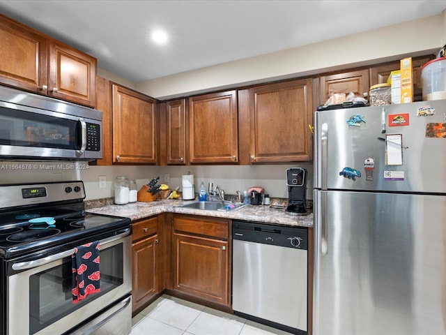 kitchen with light stone countertops, appliances with stainless steel finishes, light tile patterned floors, and sink