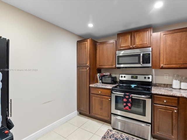 kitchen featuring light tile patterned floors, stainless steel appliances, and light stone counters