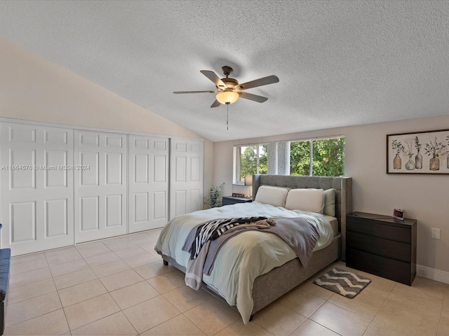 bedroom with a textured ceiling, light tile patterned flooring, vaulted ceiling, and ceiling fan