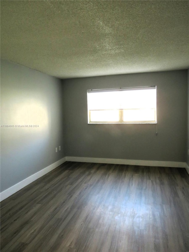 empty room featuring a textured ceiling, dark hardwood / wood-style floors, and a healthy amount of sunlight