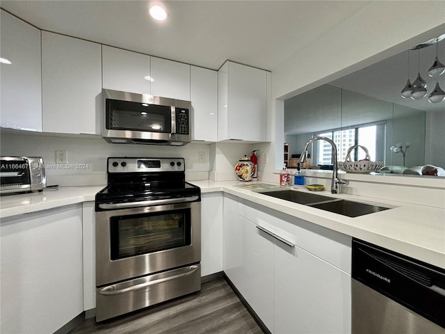 kitchen with appliances with stainless steel finishes, dark wood-type flooring, white cabinets, pendant lighting, and sink