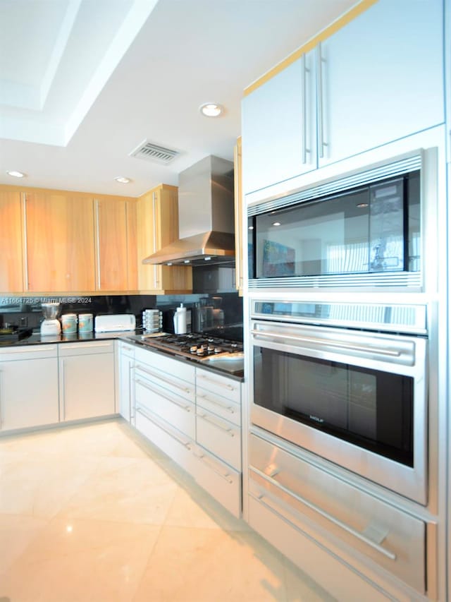 kitchen with light brown cabinets, wall chimney range hood, and stainless steel appliances