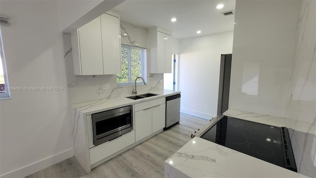 kitchen with light stone counters, stainless steel appliances, sink, light hardwood / wood-style floors, and white cabinetry