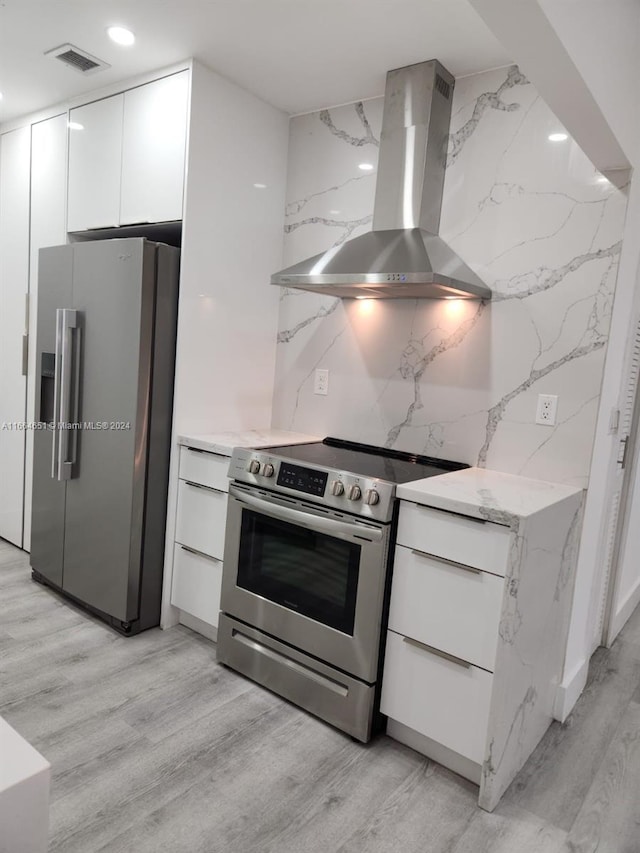 kitchen featuring white cabinets, wall chimney exhaust hood, appliances with stainless steel finishes, and light hardwood / wood-style flooring