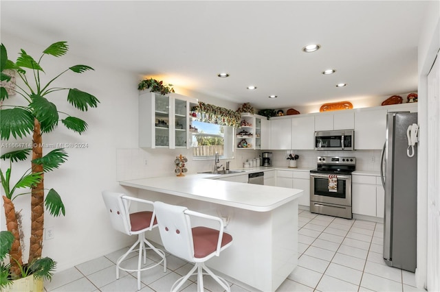 kitchen with sink, white cabinets, kitchen peninsula, appliances with stainless steel finishes, and light tile patterned floors