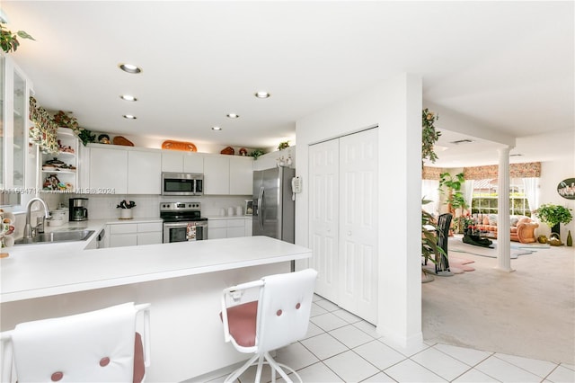 kitchen with sink, kitchen peninsula, white cabinetry, stainless steel appliances, and light carpet