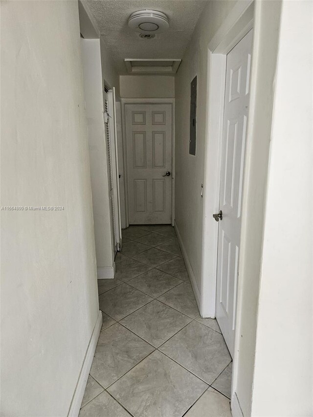 hallway with a textured ceiling, electric panel, and light tile patterned flooring