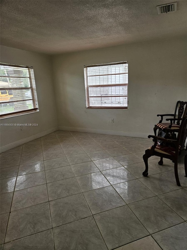 tiled spare room with a textured ceiling and a healthy amount of sunlight