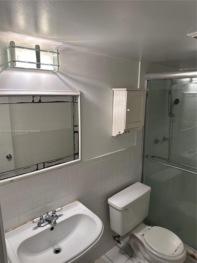 bathroom featuring sink, tile patterned floors, toilet, a shower with door, and tile walls