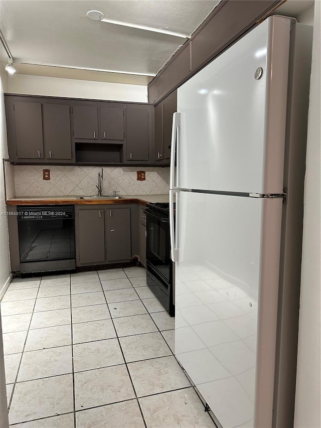 kitchen featuring backsplash, sink, light tile patterned floors, and black appliances