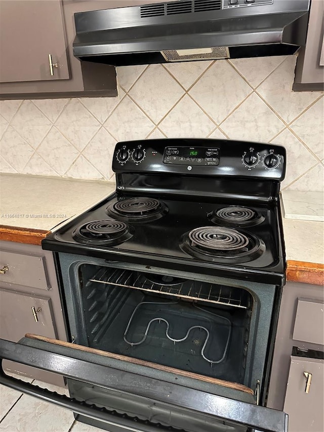 kitchen featuring ventilation hood, gray cabinetry, backsplash, and black / electric stove