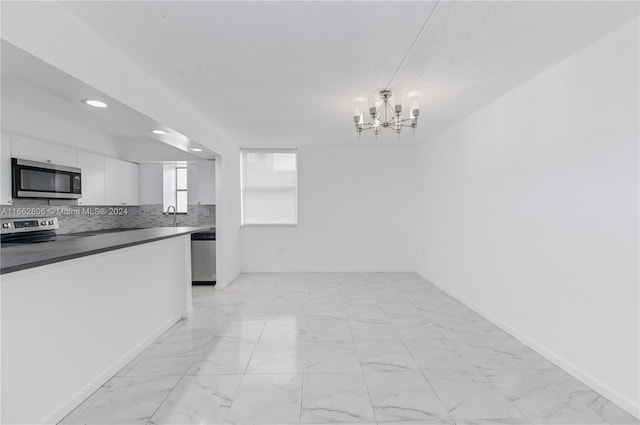 kitchen with a notable chandelier, white cabinets, hanging light fixtures, decorative backsplash, and stainless steel appliances