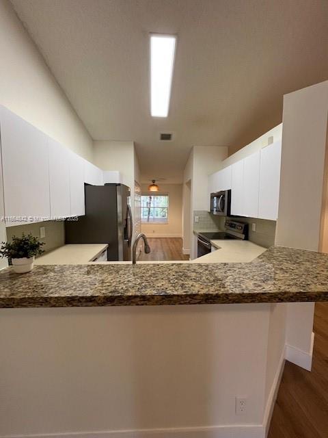 kitchen with sink, white cabinets, dark hardwood / wood-style flooring, kitchen peninsula, and stainless steel appliances