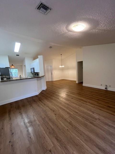 unfurnished living room with lofted ceiling, dark hardwood / wood-style floors, and a textured ceiling