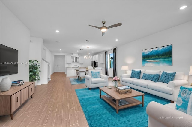 living room featuring ceiling fan with notable chandelier and light hardwood / wood-style floors