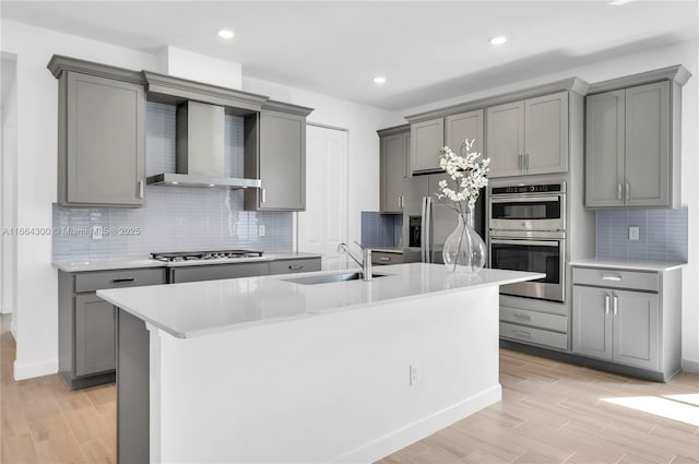 kitchen with gray cabinetry, sink, stainless steel appliances, and wall chimney exhaust hood