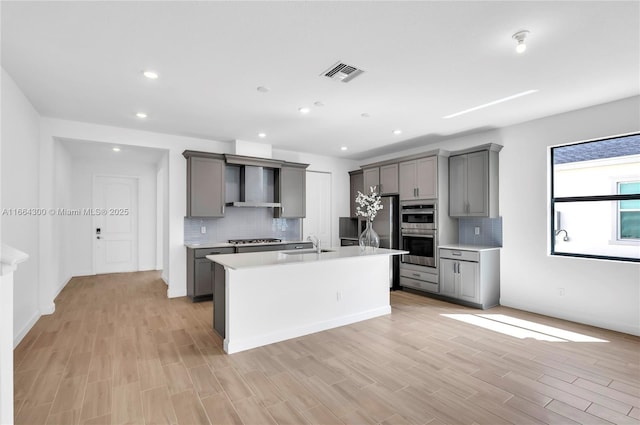 kitchen featuring gray cabinetry, a kitchen island with sink, and appliances with stainless steel finishes