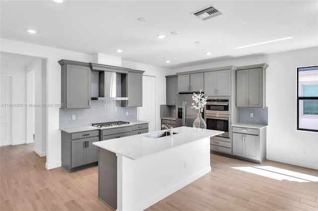 kitchen featuring appliances with stainless steel finishes, gray cabinetry, wall chimney range hood, and sink