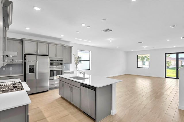 kitchen with an island with sink, stainless steel appliances, gray cabinets, and sink