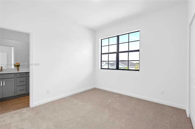 unfurnished bedroom featuring connected bathroom, sink, and light colored carpet