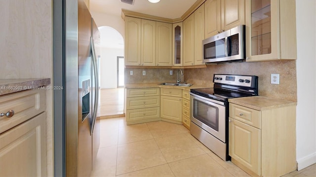 kitchen with backsplash, light tile patterned floors, stainless steel appliances, light brown cabinetry, and sink