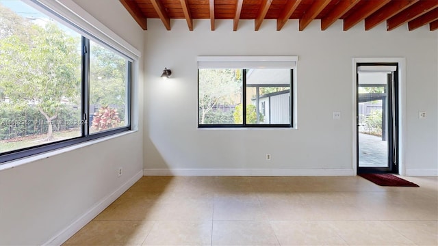 empty room featuring beam ceiling, light tile patterned flooring, and a healthy amount of sunlight