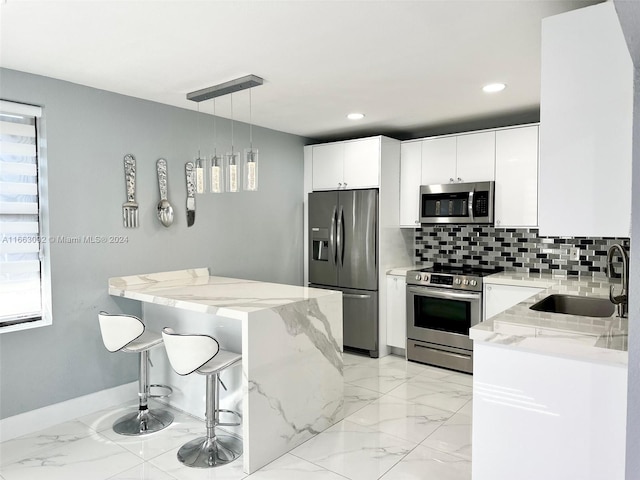 kitchen featuring hanging light fixtures, sink, white cabinetry, stainless steel appliances, and light stone countertops