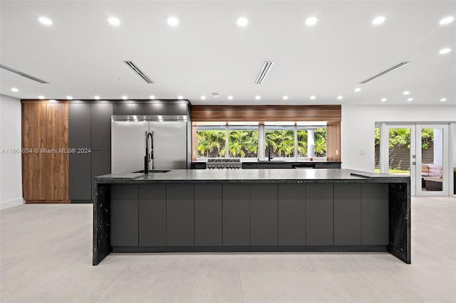 kitchen featuring stainless steel appliances, dark stone countertops, a large island with sink, and sink