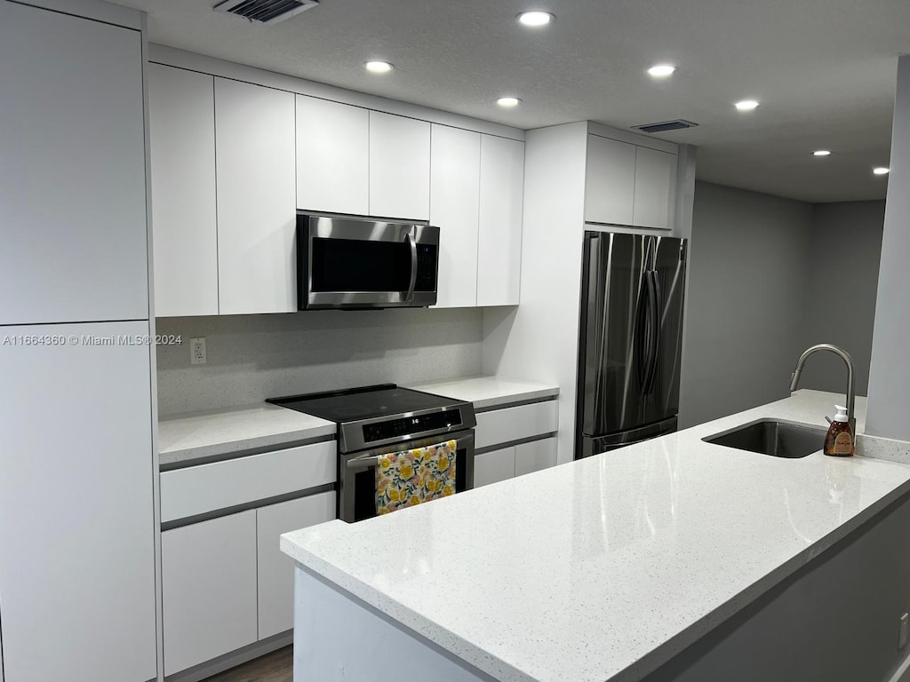 kitchen featuring light stone counters, appliances with stainless steel finishes, sink, and white cabinetry