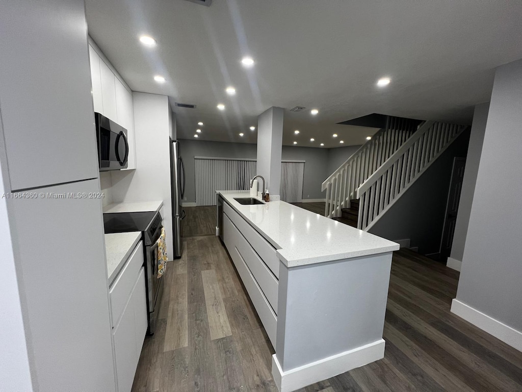 kitchen with sink, a large island with sink, white cabinetry, appliances with stainless steel finishes, and dark hardwood / wood-style floors