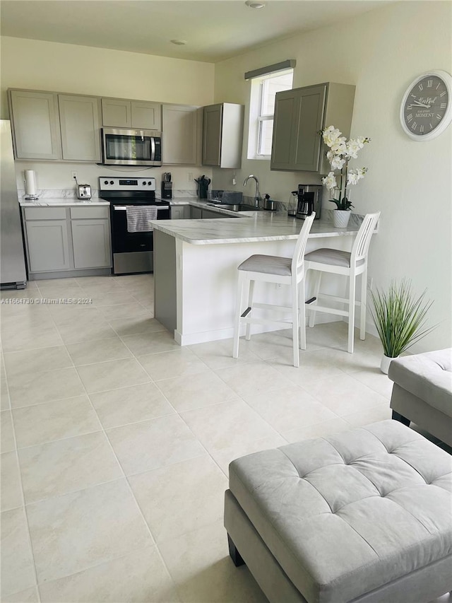 kitchen featuring sink, kitchen peninsula, a kitchen bar, stainless steel appliances, and light tile patterned floors