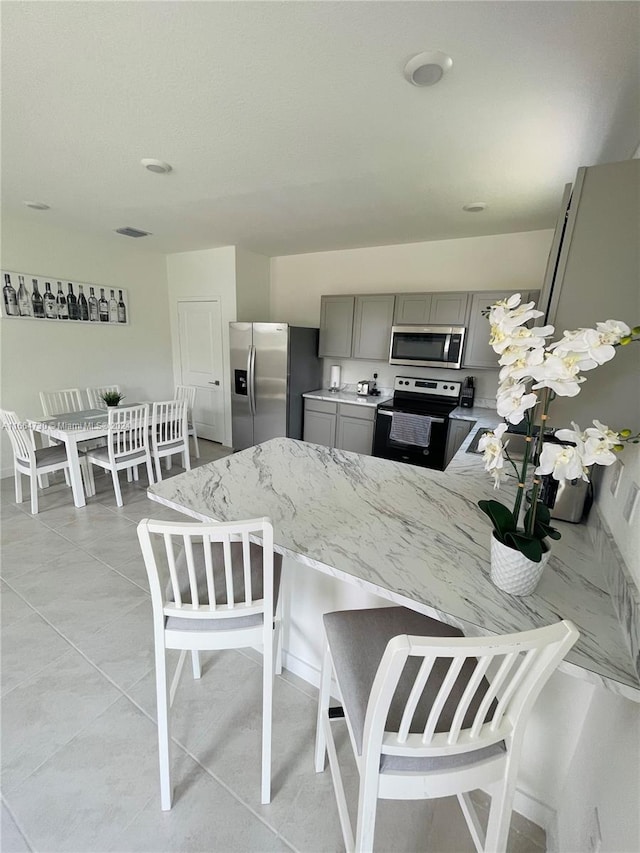 kitchen featuring appliances with stainless steel finishes, kitchen peninsula, light stone countertops, and gray cabinets