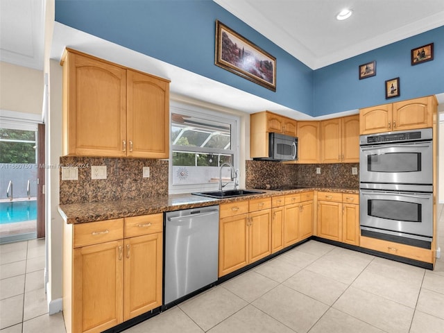 kitchen featuring appliances with stainless steel finishes, light tile patterned flooring, dark stone counters, ornamental molding, and sink