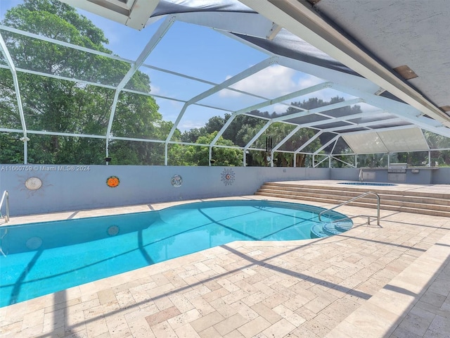 view of pool with an outdoor kitchen, glass enclosure, and a patio area