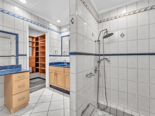 bathroom featuring tile walls, tiled shower, vanity, crown molding, and tile patterned floors