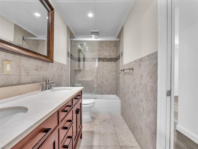 full bathroom with bath / shower combo with glass door, vanity, tile walls, and toilet