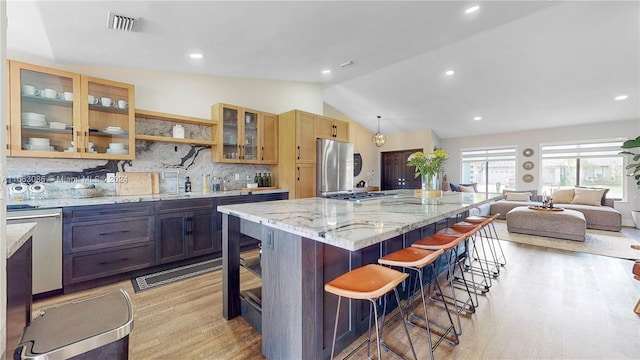 kitchen with light hardwood / wood-style floors, stainless steel appliances, a kitchen bar, lofted ceiling, and a spacious island