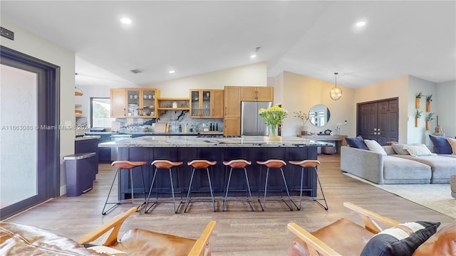 kitchen with lofted ceiling, stainless steel fridge, a kitchen island, a breakfast bar area, and light hardwood / wood-style floors