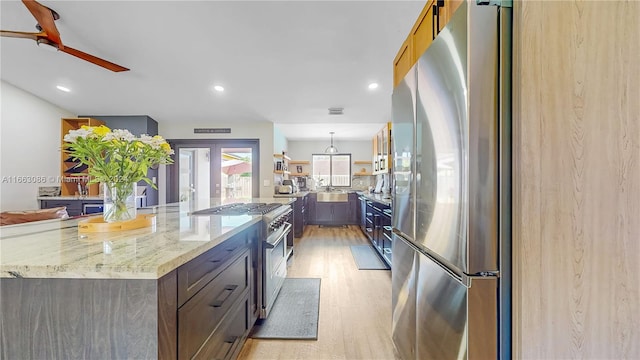 kitchen featuring hanging light fixtures, light stone countertops, stainless steel appliances, light wood-type flooring, and ceiling fan