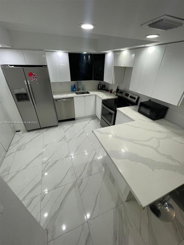 kitchen with light stone counters, sink, stainless steel appliances, and white cabinets