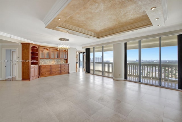 unfurnished living room with a tray ceiling, an inviting chandelier, ornamental molding, and a wall of windows